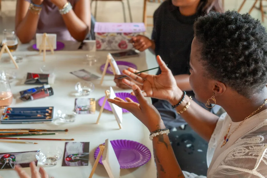 Friends talking across a table set with small canvases and paints