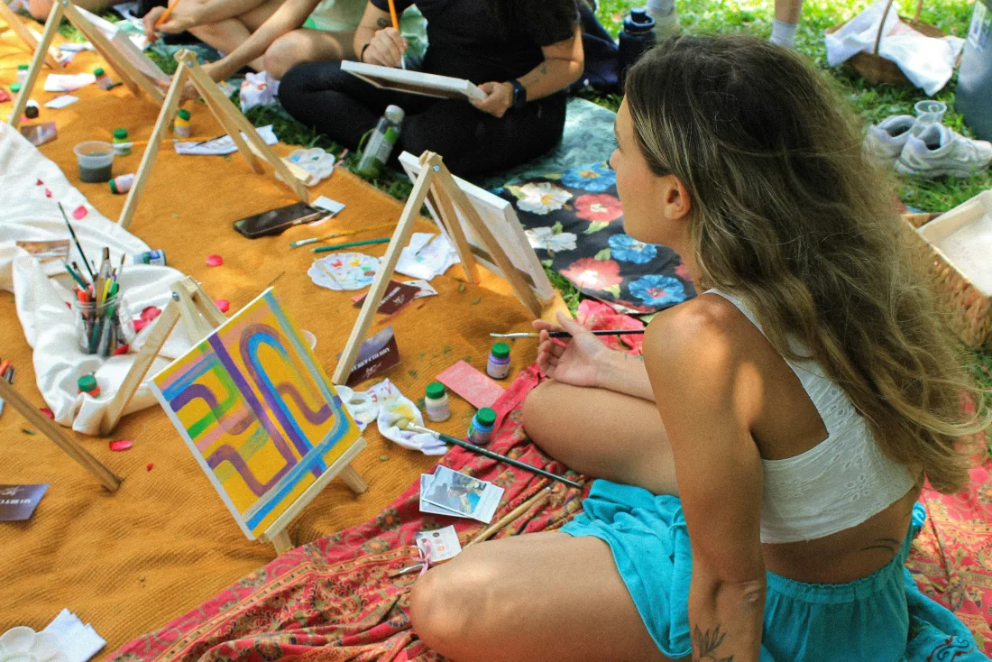 Friends painting colorful canvases at an outdoor picnic table